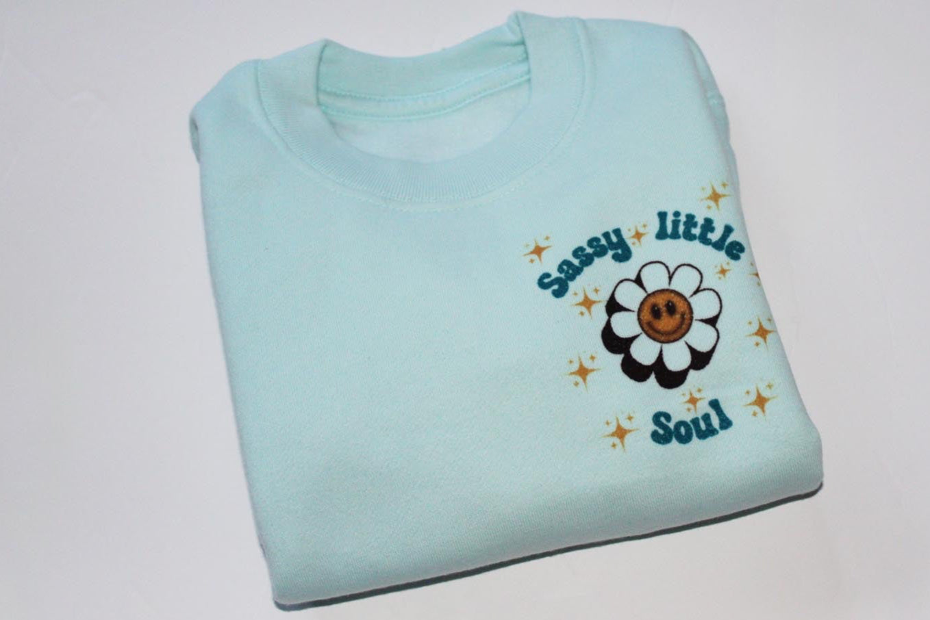 kids blue sassy little soul sweatshirt in blue. Stars around the writing which is on the right hand side of the top. It has a flower smiley face in the middle of the writing.