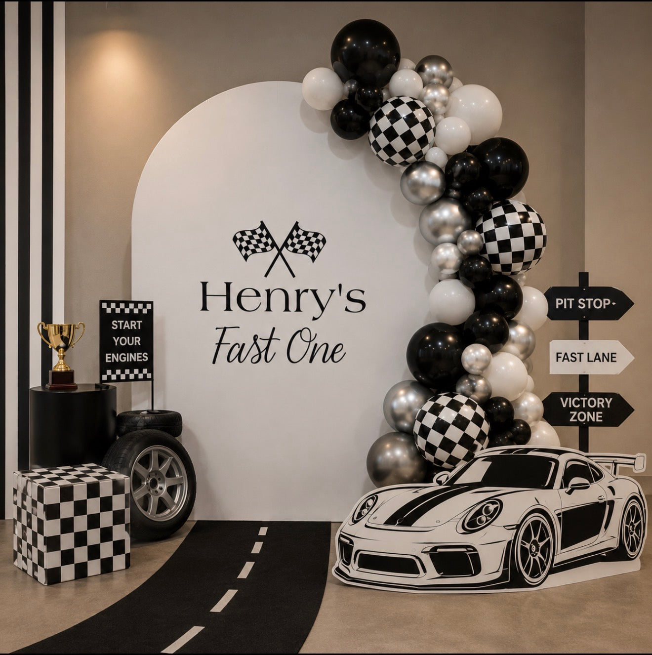 Decorated birthday setup with 'Henry's First One' theme, including balloons, car cutout, and checkered elements.